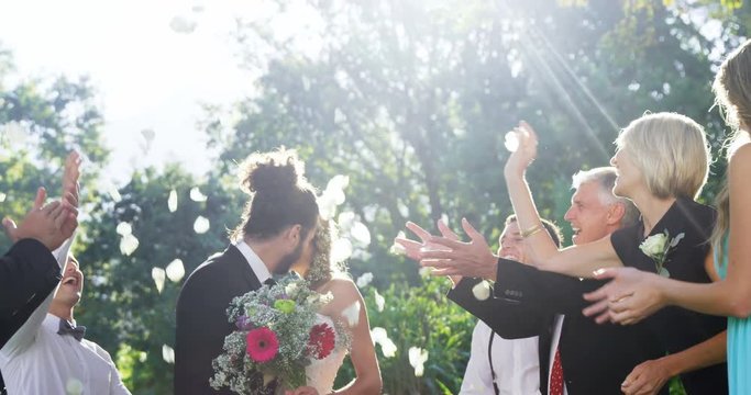 Guests toss petals while bride and groom kissing  