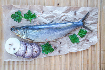 Delicious salted herring with red onion, salt and pepper on the old bamboo background.
