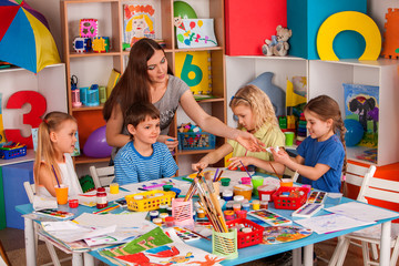 Fototapeta premium Kids playroom organization of children painting and drawing in kid's club. Craft lesson in primary school. Teaching children to do common project.