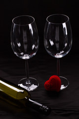 Two wine glasses, bottle and gift box. Two empty wine glasses and small heart shaped velvet gift box on black background. Beautiful gift for Valentines Day.