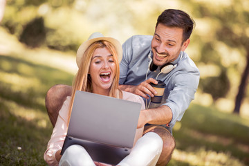 Young couple sitting on the grass and using laptop.