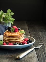Pancakes with fresh berries, mint and honey on plate and wooden table. Close up with copy space.