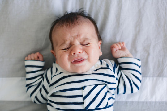 Newborn baby boy crying lying on bed at home.