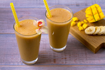 Mango banana smoothie on wooden background, horizontal