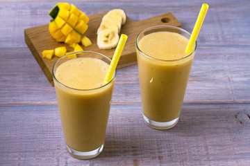 Mango banana smoothie on wooden background, horizontal