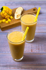Mango banana smoothie on wooden background, vertical