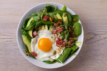 Fried egg with bacon, quinoa, avocado, spinach and pumpkin seeds for breakfast