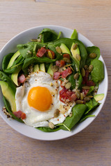 Fried egg with bacon, quinoa, avocado, spinach and pumpkin seeds for breakfast
