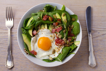 Fried egg with bacon, quinoa, avocado, spinach and pumpkin seeds for breakfast
