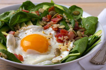 Fried egg with bacon, quinoa, avocado, spinach and pumpkin seeds for breakfast