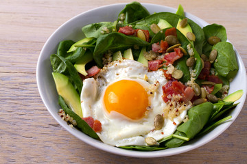 Fried egg with bacon, quinoa, avocado, spinach and pumpkin seeds for breakfast