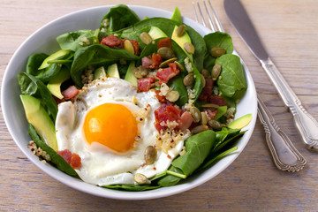 Fried egg with bacon, quinoa, avocado, spinach and pumpkin seeds for breakfast
