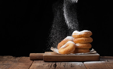 Baker sprinkles sweet donuts with powder sugar on black background. Delicious, but unhealthy food...
