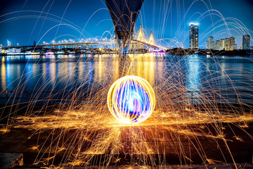 Hot Golden Sparks Flying from Man Spinning Burning Steel Wool under Bhumibol Bridge in Bangkok...