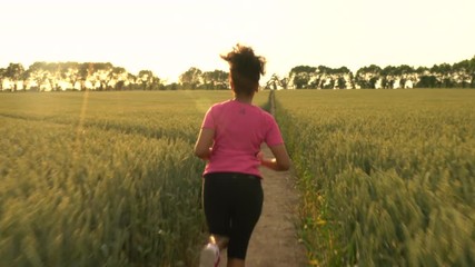 4K video clip of beautiful healthy mixed race African American girl teenager female young woman runner running on path through field of barley or wheat crops at sunset