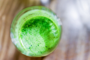 Macro closeup flat top view of bubble surface of green juice smoothie in glass with wooden background