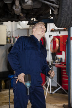 Mechanic With Hand Tools Examining Car In Garage