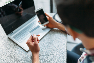 A man sits in a cafe with a laptop, make purchases via the online store, payment by credit card, a plastic card