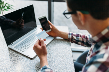 A man sits in a cafe with a laptop, make purchases via the online store, payment by credit card, a plastic card