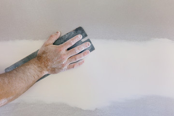 Man's hand sanding plasterboard in home renovation