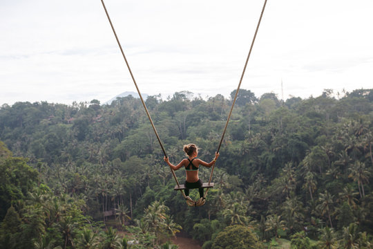 Brave young girl on hgh swing over tropical valley