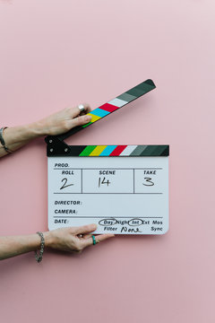 Woman holding clapperboard over pink background