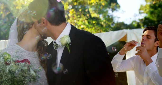 Bride and groom kissing while guest blowing bubbles  
