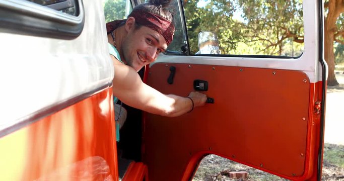 Man opening door of camper van and smiling towards camera 