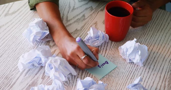 Female executive writing on sticky notes while having coffee  