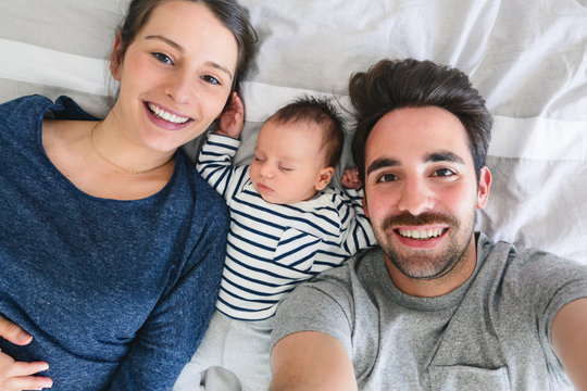 Young family with newborn baby taking a selfie at home.