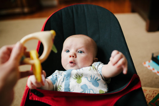 infant focusing on a rattle held in front of him by his mother