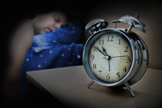 a man sleeping on the bed beside the alarm clock on table, in night.