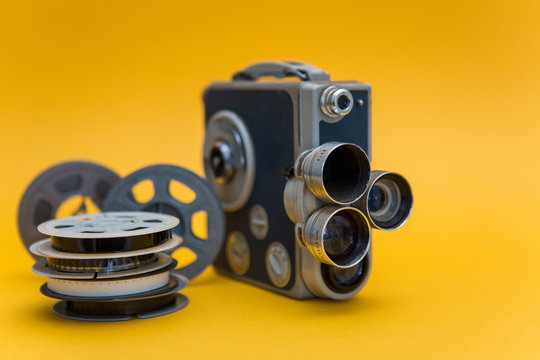 Vintage cinema camera and reels over yellow background