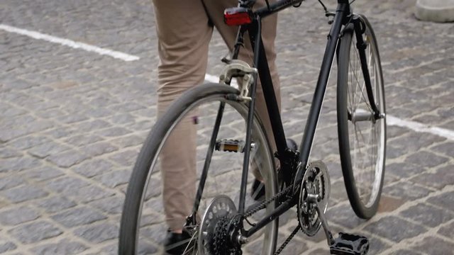 Closeup 4k video of young stylish man walking with bicycle, sitting on it and riding away