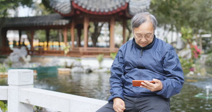 Asian old man use of mobile phone and sitting at chinese garden