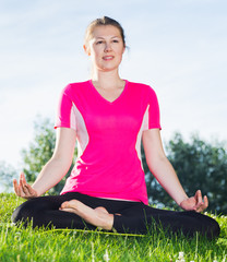 Smiling adult woman in pink T-shirt is sitting and meditating