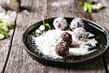 Homemade healthy vegan chocolate balls, truffles, candies sprinkled grated coconut in the plate on the vintage wooden table. Selective focus 