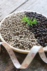 black and white pepper corn side by side with measuring tape on wooden table ,diet concept nutrition.