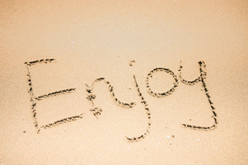 Enjoy word is written on the beach sand