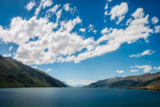 Simple Perspective background, only water, hills and puffy clouds in the sky, at Lake Wakatipu in the Southern Island of New Zealand.