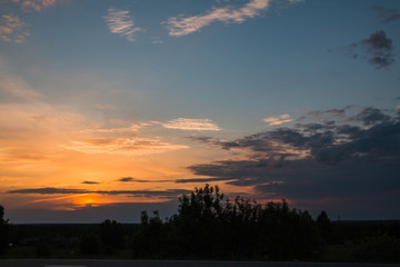 Sunset, clouds on the sky and dark trees