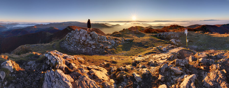Sunrise with inversion above the deep autumn valley of mountains with small man on the top, who is watching this beautiful scenery