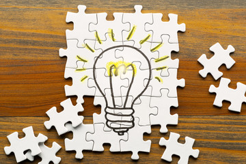 Idea creation. Light bulb drawn on puzzle. Puzzle pieces on wooden desk.
