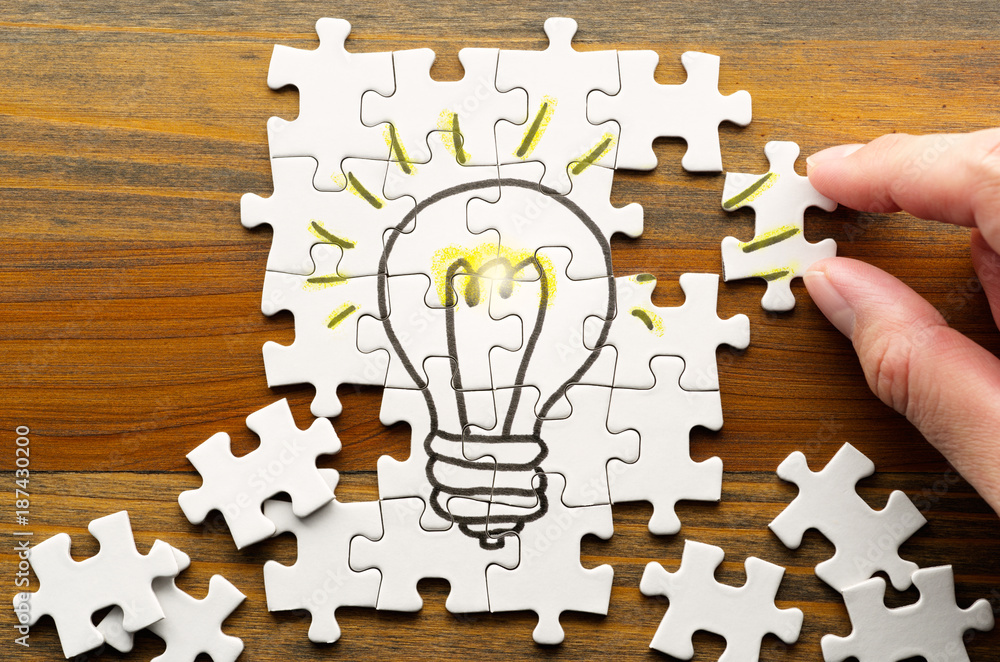 Aufkleber Finding solution. Solving puzzle on wooden desk. Idea creation. Light bulb drawn on puzzle.
