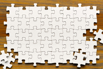 White puzzle pieces on wood background. Partially completed box shaped puzzle pieces.
