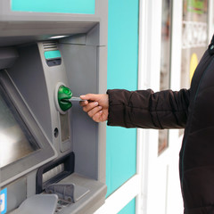 Hand inserting ATM card into bank machine to withdraw money