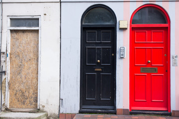 Black door next to a red door and a wooden panel replacing a missing door in the front facade of a Victorian British English house