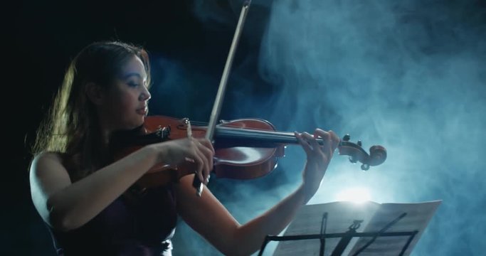 a talented girl violinist performs at her first solo concert, stage light, dark background