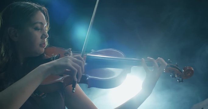 a talented girl violinist performs at her first solo concert, stage light, dark background