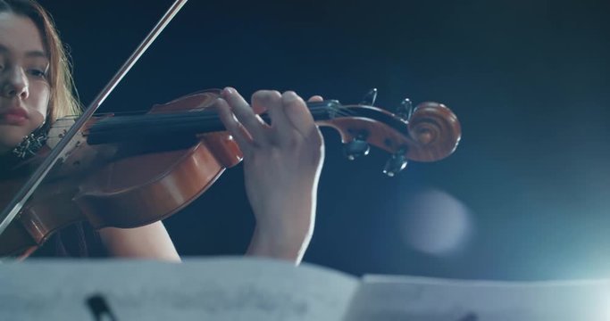 detail shot, performance of violinist girl on stage, light, dark background